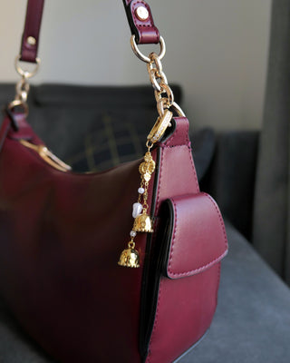 Gold jhumka bag charm hanging elegantly from a stylish handbag, blending traditional South Asian jewelry design with modern fashion accessories.